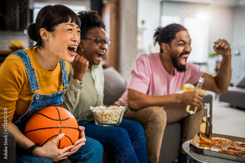 Multiracial group of friends watching basketball game, eating pizza, drinking beer and cheering.