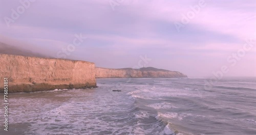 Cliffs and lighthouse at sunset with foam near the shore. Sea surface aerial view of sea. Puerto Eten, Peru.
