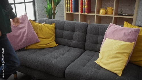 Bearded man sitting on grey couch with yellow and pink pillows feeling stressed in a modern living room photo