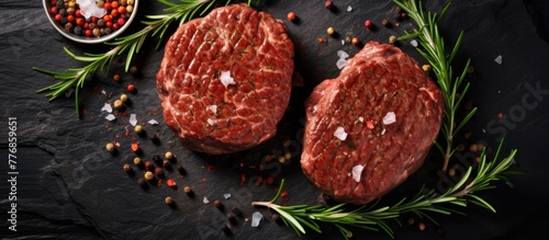 A pair of cooked steaks placed on a dark stone surface, garnished with fresh rosemary herbs