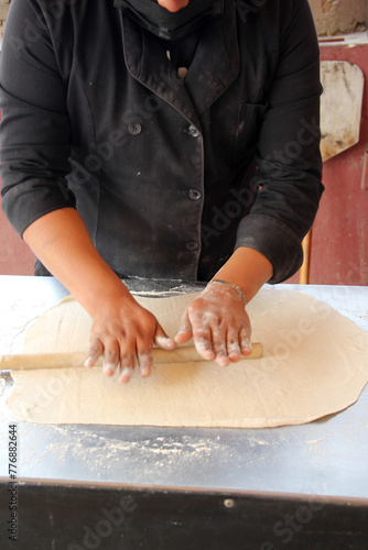 Hands of pizza maker man kneads dough, prepares and shapes for pizza base with rolling pin and flour