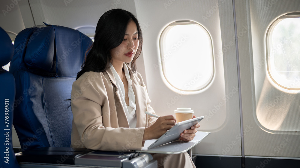Fototapeta premium A hard-working businesswoman focus on her work on her tablet while flying for a business meeting.