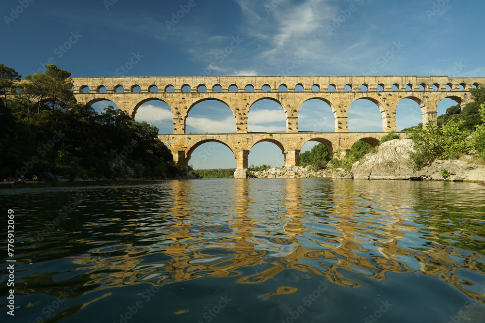 Pont du Gard famous aqueduct arched bridge mirroring in Gardon river, popular tourist landmark in France