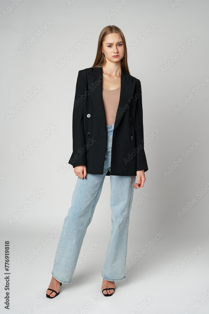 Young Woman Wearing Black Jacket and Jeans posing on gray background studio shot . Young Woman Wearing Black Jacket and Jeans posing on gray background studio shot .