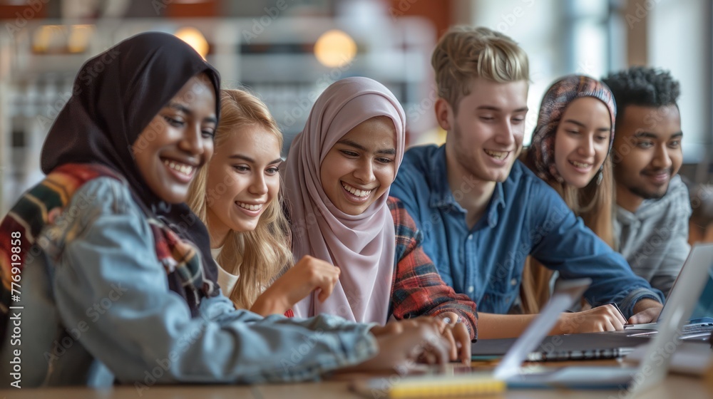 A happy diverse group of students collaborating on a project using a laptop in class A happy diverse group of students collaborating on a project using a laptop in class