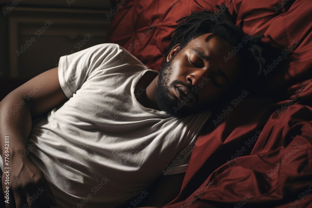 Portrait of an African American man, around 35 years old, lying on the bed in the bedroom, holding his stomach due to cramps Portrait of an African American man, around 35 years old, lying on the bed in the bedroom, holding his stomach due to cramps