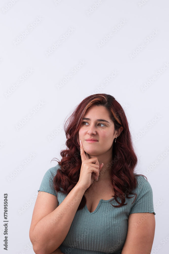 Vertical portrait of a smiling young woman with her hand resting on her face and looking to the side with an expression of having an idea. Clear background and copy space. Vertical portrait of a smiling young woman with her hand resting on her face and looking to the side with an expression of having an idea. Clear background and copy space.