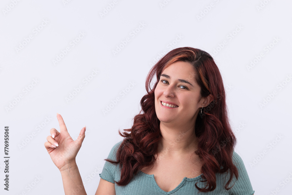 Horizontal portrait of a beautiful woman smiling and pointing her finger upwards. Light background and copy space. Promotion and marketing concept Horizontal portrait of a beautiful woman smiling and pointing her finger upwards. Light background and copy space. Promotion and marketing concept