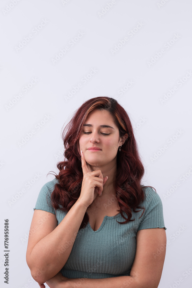 Vertical portrait of a pensive young woman with her hand resting on her face with thoughtful gesture and looking down. Light background and copy space. Promotion and marketing concept Vertical portrait of a pensive young woman with her hand resting on her face with thoughtful gesture and looking down. Light background and copy space. Promotion and marketing concept