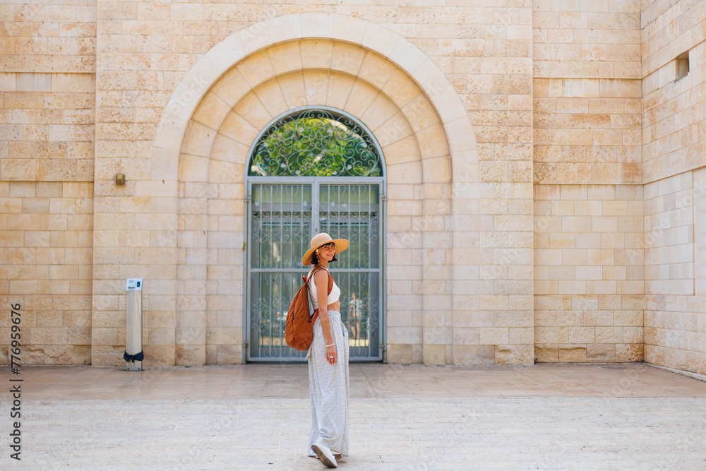 A stylish fashionable girl traveler in a brown hat with a backpack stands in front of an old house while traveling. visiting a museum while traveling.