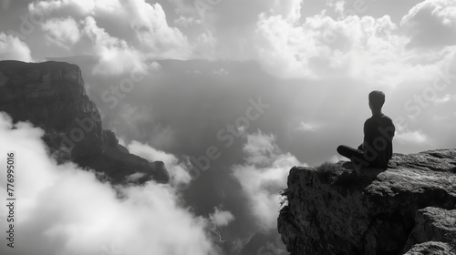 Black and white images that capture moments of solitude Where a person sits on the edge of a cliff overlooking a vast valley filled with clouds below. © VRAYVENUS
