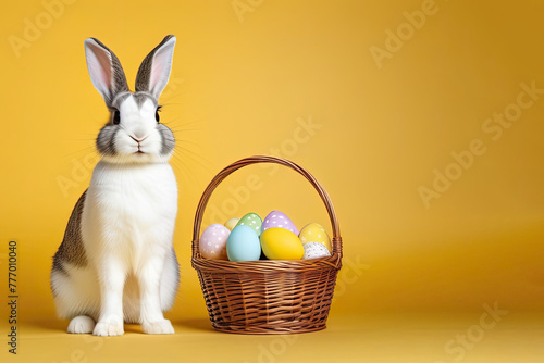 portrait of funny rabbit with basket of eggs on yellow background, Easter.
