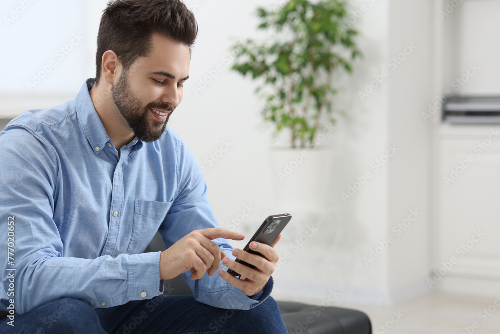 Handsome young man using smartphone in office, space for text Handsome young man using smartphone in office, space for text