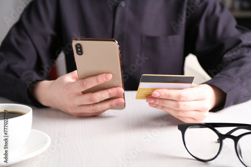 Online payment. Woman with smartphone and credit card at white wooden table, closeup