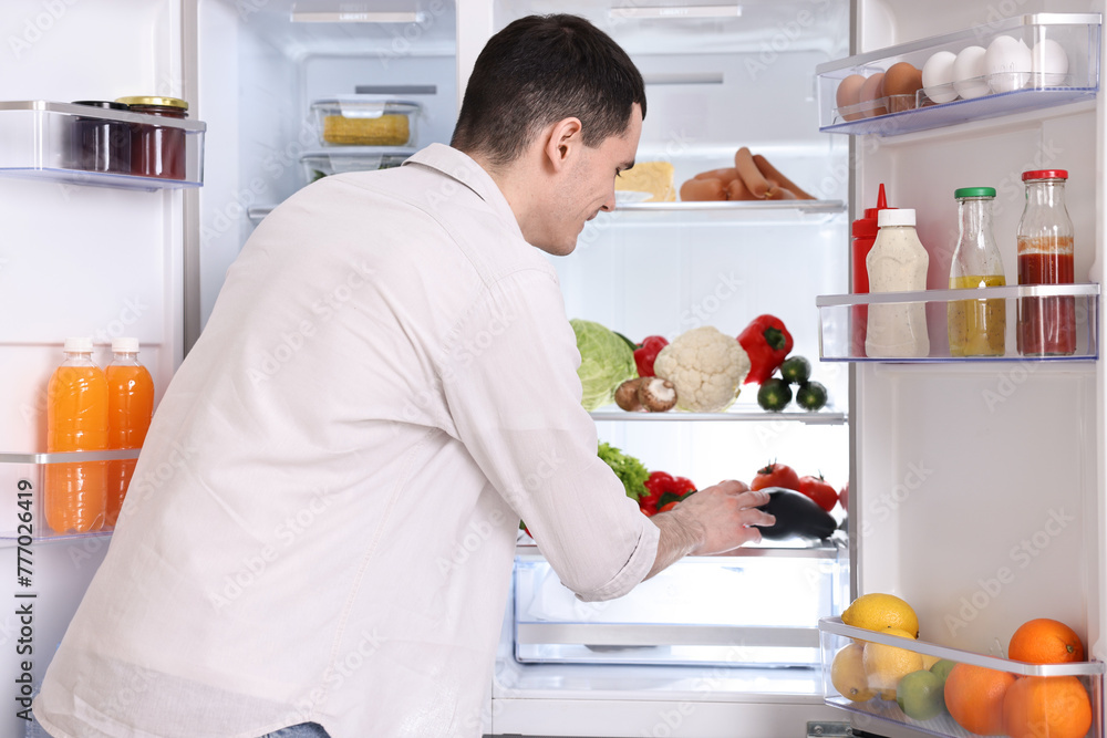 Happy man taking eggplant out of refrigerator in kitchen Happy man taking eggplant out of refrigerator in kitchen