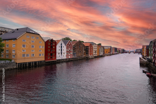 Colorful Stilt houses line the peaceful River Nidelva in Trondheim Brygge district under a vibrant evening sunset sky. Tourist travel destination in Trøndelag Norway photo