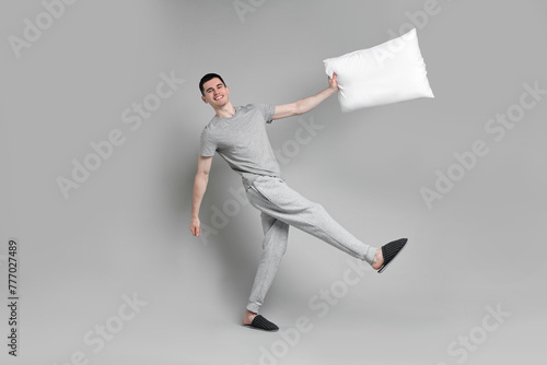 Happy man in pyjama holding pillow on grey background