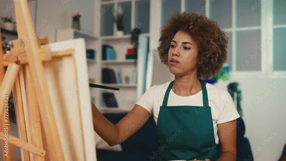 Thoughtful woman artist painting a picture at easel stand, looking for ideas Thoughtful woman artist painting a picture at easel stand, looking for ideas