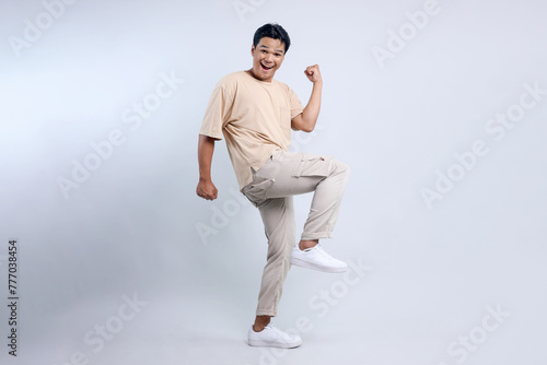 Full length view of cheerful Asian man clenched fist and dancing rejoicing victory isolated on white background