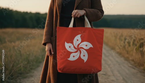 A woman stands in a field, holding a shopper bag adorned with the Hong kong flag, promoting the idea of locally sourced, eco-friendly produce photo