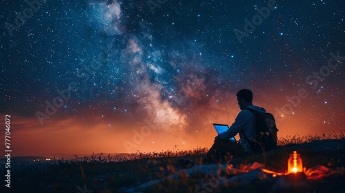 A man is sitting on a hillside  looking up at the stars. He is holding a laptop and he is enjoying the peacefulness of the night sky