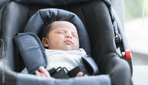 Portrait of adorable less than one month old newborn baby girl sleeping in the modern car seat with fastening safety belt. Selective focus on little Asian Australian child