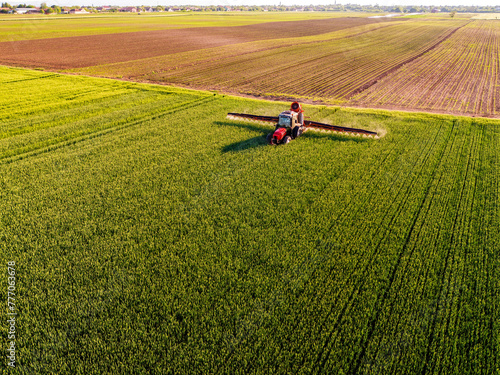 Drone shot of a tractor with sprayer in action on a vibrant green wheat farmland