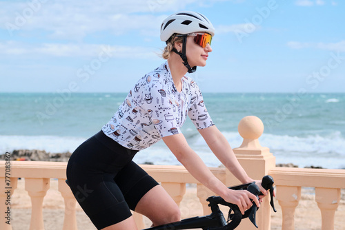 Beautiful woman cyclist wearing cycling kit and helmet riding a bicycle near the sea with amazing view. Cycling adventure in Spain. Calpe, Alicante, Spain.
