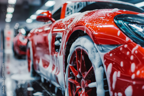 Red Sports car Wheels Covered in Shampoo Being Rubbed by a Soft Sponge at a Stylish Dealership Car Wash. Performance Vehicle Being Washed in a Detailing Studio © VisualProduction
