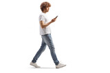 Full length profile shot of a casual guy with curly hair walking and using a smartphone