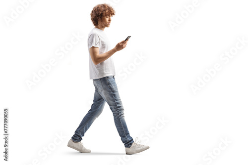 Full length profile shot of a casual guy with curly hair walking and using a smartphone