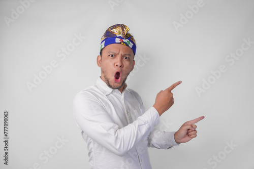 Surprised Balinese man in white shirt and traditional headdress called udeng pointing to the copy space on the left and right side photo