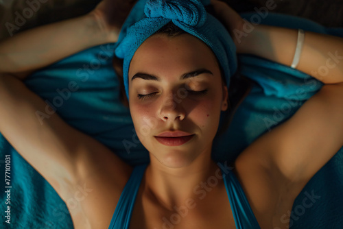 A beautiful woman in a blue tank top and nightcap lying on her back with her eyes closed getting a massage 