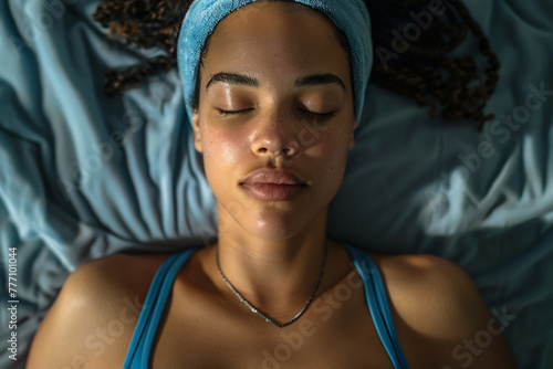 A beautiful woman in a blue tank top and nightcap lying on her back with her eyes closed getting a massage 
