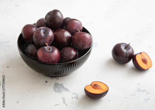 Bowl with raw ripe purple plums on light kitchen background.