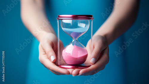 Woman's hand holding an hourglass on blue and pink background © Yuwarin