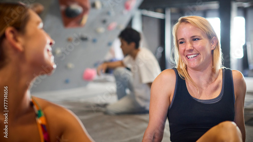 Close Up Of Two Women Taking A Break And Talking By Climbing Wall In Indoor Activity Centre