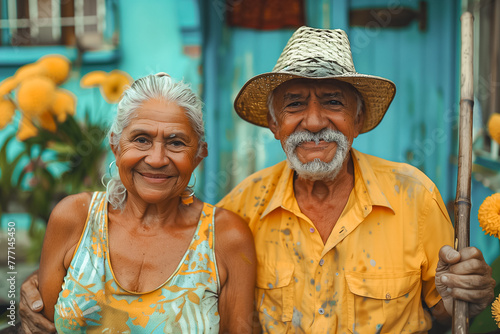 Joyful elderly couple standing close with a backdrop of a blue house and tropical plants, exuding warmth © Jelena