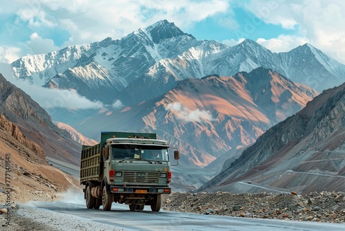 The truck drives along a mountain road with snow-capped peaks in the distance and a beautiful sky.