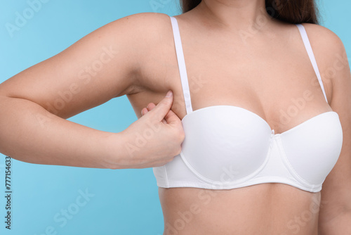 Mammology. Woman in bra doing breast self-examination on light blue background, closeup