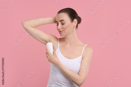 Beautiful woman applying deodorant on pink background