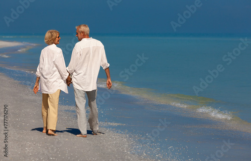 Happy senior couple walking smiling holding hands on an empty tropical beach