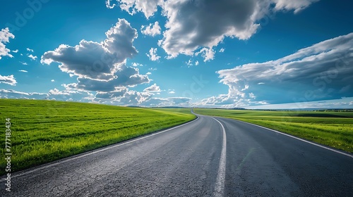 Asphalt road in green fields on blue cloudy sky background