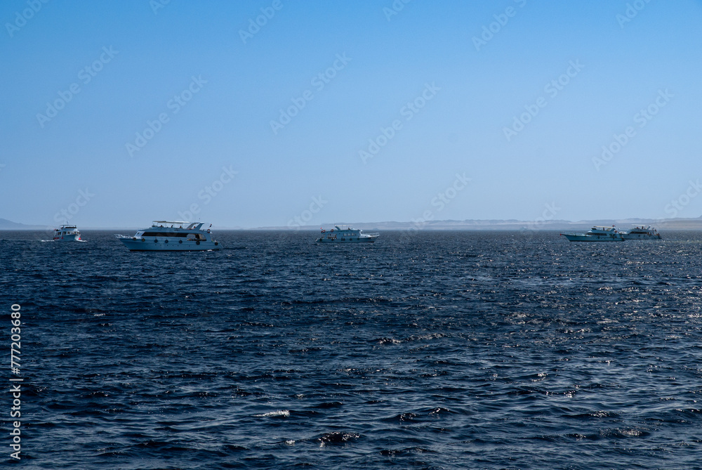 White yachts with tourists are moving on open sea. Yacht hulls cut through turquoise waters of Red Sea. Horizon line separates sea and sky. Sharm el-Sheikh, Egypt, April 20, 2008