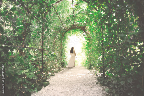 elegant young woman walks happily towards the exit of a tunnel formed by lush plants