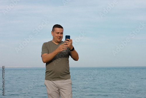 a man speaks on a video call on the phone against the backdrop of the sea and sky on the beach