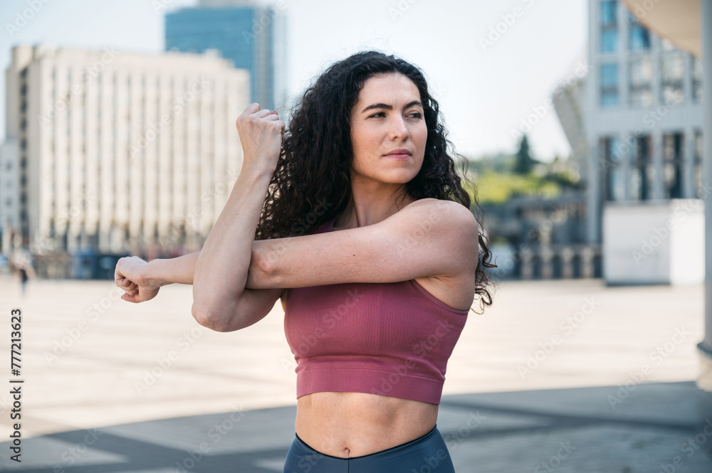 Fototapeta premium Waist portrait of athletic young woman warming up, stretching arms outdoors