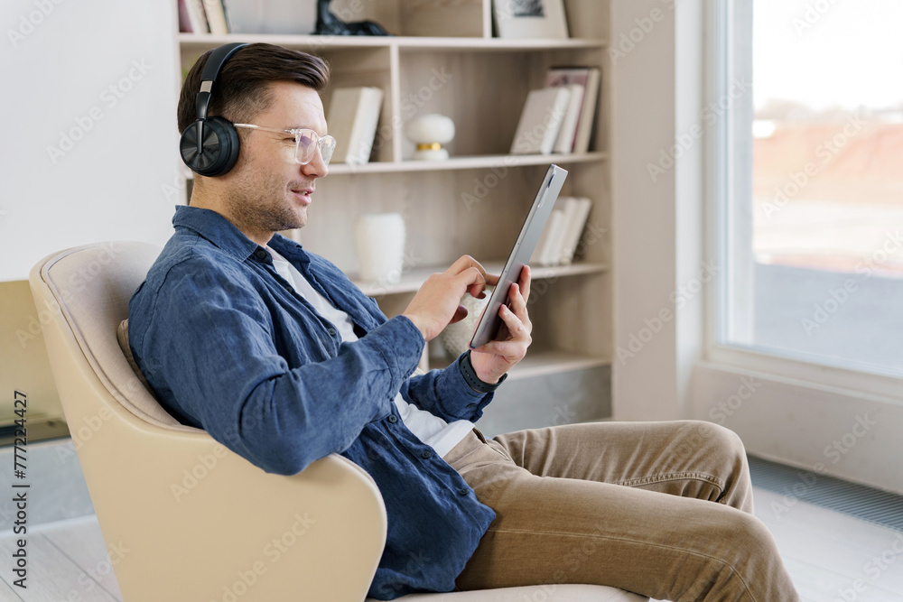 A man enjoys his leisure time with headphones and a tablet in a minimalist chair, epitomizing modern relaxation and comfort.