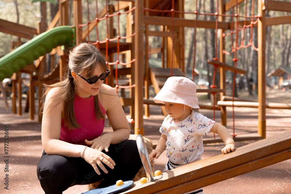 Fototapeta premium happy mother plays and pushes her child on a swing in the park on a hot spring day