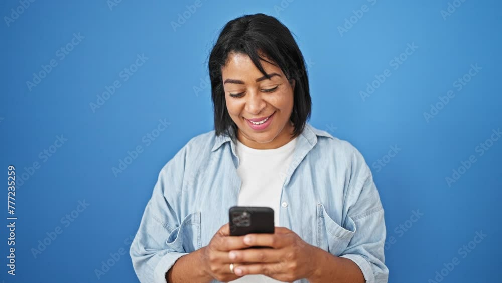 Smiling hispanic woman using smartphone against vibrant blue background illustrates technology engagement Smiling hispanic woman using smartphone against vibrant blue background illustrates technology engagement